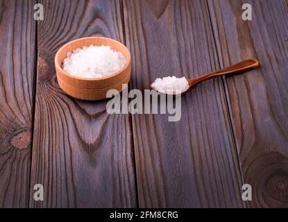 Bagnare il sale bianco in una ciotola di legno con un cucchiaio su un tavolo di legno Foto Stock