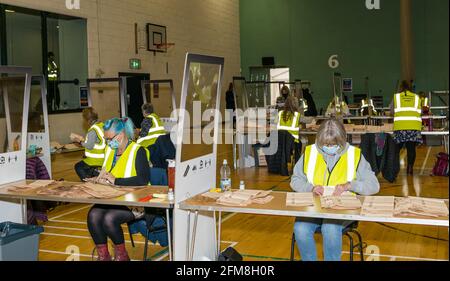 Centro sportivo Meadowmill, East Lothian, Scozia, Regno Unito. 7 maggio 2021. Conteggio delle elezioni del parlamento scozzese per la circoscrizione di East Lothian: Il personale di funzionario che ritorna indossando una maschera faccia ordina le schede elettorali e conta i voti Foto Stock