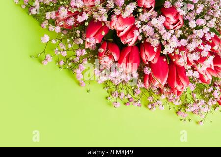 Tulipani rossi e fiori di gypsophila bouquet su sfondo verde, fuoco selettivo. Festa della mamma, concetto di festa di compleanno. Vista dall'alto, spazio di copia Foto Stock