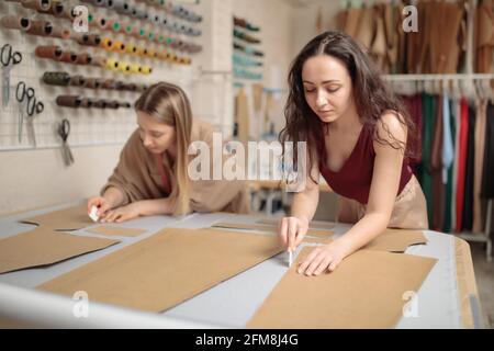 giovani sarti concentrati utilizzando modelli di cucitura mentre si lavora alla creazione di giacca maschile su misura Foto Stock