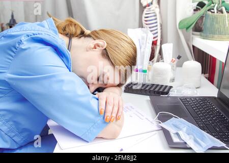 Stanco medico femminile di mezza età lavora su un computer portatile. Studio medico, attrezzature mediche. Foto Stock