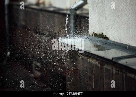 gocce di pioggia cadenti si rompono sulla sporgenza. spruzzi da acqua corrente. tubo di scarico dal tetto di un edificio durante una tempesta di pioggia Foto Stock