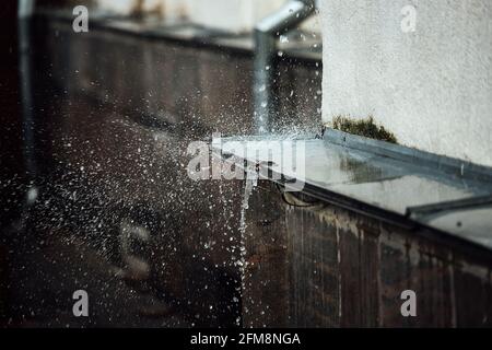 gocce di pioggia cadenti si rompono sulla sporgenza. spruzzi da acqua corrente. tubo di scarico dal tetto di un edificio durante una tempesta di pioggia Foto Stock