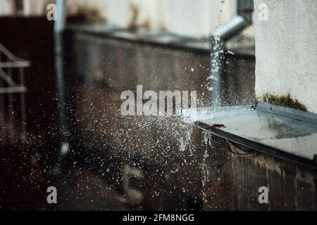 gocce di pioggia cadenti si rompono sulla sporgenza. spruzzi da acqua corrente. tubo di scarico dal tetto di un edificio durante una tempesta di pioggia Foto Stock