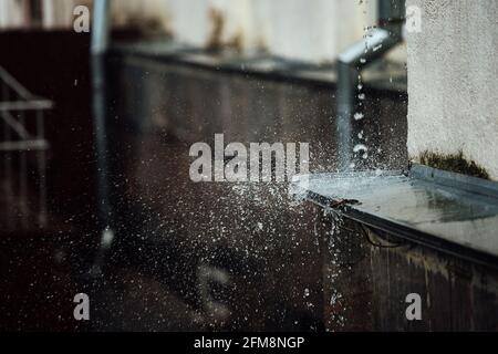 gocce di pioggia cadenti si rompono sulla sporgenza. spruzzi da acqua corrente. tubo di scarico dal tetto di un edificio durante una tempesta di pioggia Foto Stock