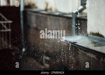 gocce di pioggia cadenti si rompono sulla sporgenza. spruzzi da acqua corrente. tubo di scarico dal tetto di un edificio durante una tempesta di pioggia Foto Stock