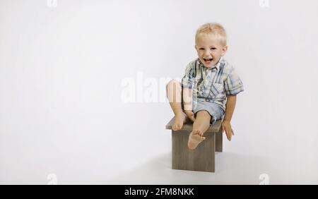 Allegro ragazzo caucasico seduto su una sedia di legno isolato su sfondo bianco Foto Stock