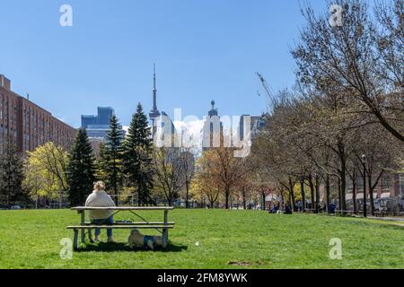 Persone reali che si rilassano in un parco di Toronto durante i tempi della pandemia di Coronavirus o Covid-19. Lo skyline della città con la CN Tower è visto nel bac Foto Stock