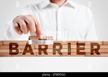 Uomo d'affari costruisce una struttura di blocchi di legno con la parola barriera. Costruire un concetto di barriera. Foto Stock