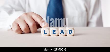 Uomo d'affari premendo il dito sui cubetti di legno con la parola piombo. Concetto di leadership organizzativa o di mercato. Foto Stock