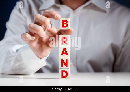 Uomo d'affari mette un cubo sulla cima di cubetti di legno a più livelli con la parola marca. Concetto di business di brand building. Foto Stock