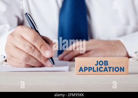 Applicazione di lavoro scritta su un blocco di legno con un uomo d'affari che scrive su un foglio di carta. Concetto di assunzione, colloquio o valutazione dei candidati. Foto Stock