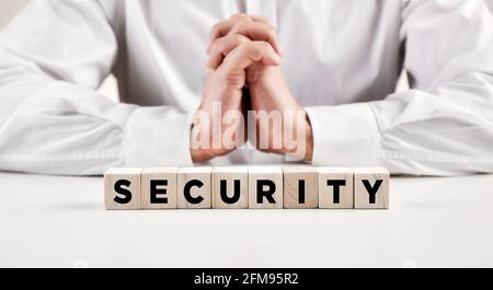 La parola sicurezza scritta su un blocco di legno con un uomo d'affari con le mani incrociate. Foto Stock
