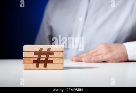 Icona hashtag scolpito su blocchi di legno con un uomo d'affari sullo sfondo. Concetto di marketing social media aziendale. Foto Stock