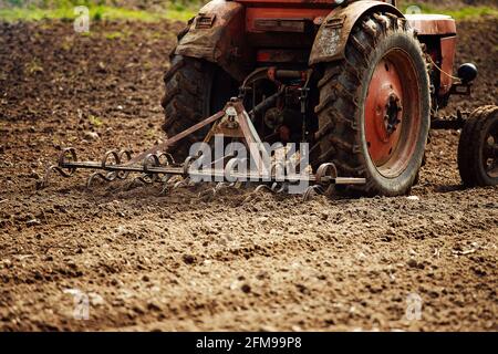 aratro trattore aratura la terra per piantare piante agricole. il coltivatore coltiva la terra in primavera per seminare semi. aratro di ferro del meccaniz Foto Stock