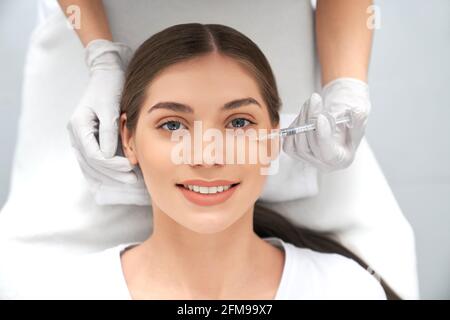 Vista dall'alto ritratto di sorridente bella giovane donna bruna sulla procedura per miglioramenti della pelle. Concetto di processo stringere la pelle dalle rughe in estetista professionista. Foto Stock
