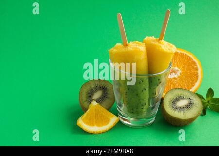 Popsicle con kiwi e frutta arancione su sfondo verde. Spazio di copia. Foto Stock