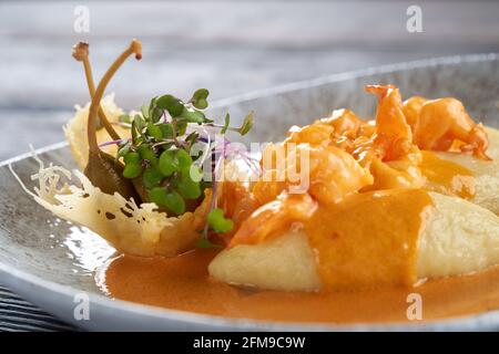 Closeup di gamberi cucinati nel ristorante per cena. Deliziosi frutti di mare esotici con salsa d'arancia sul piatto, tre cotolette di patate servite con verdure e frutti di bosco. Concetto di cibo e cucina. Foto Stock