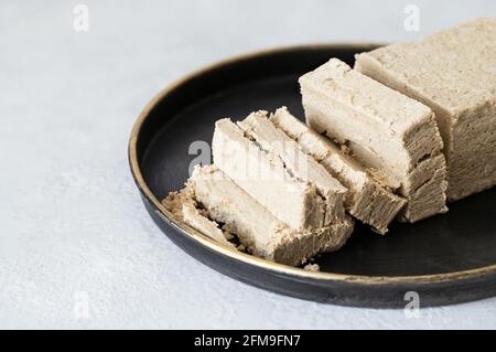 Halva affettato in un piatto nero su sfondo bianco. Primo piano dell'halva di girasole. Dessert orientale. Foto Stock