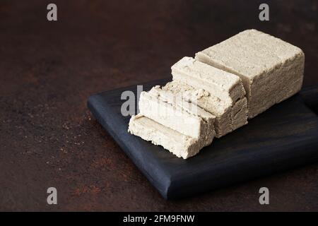 Tagliata a fette di halva su un vassoio di legno su sfondo marrone. Dolci orientali. Dessert vegetariano. Spazio di copia. Foto Stock