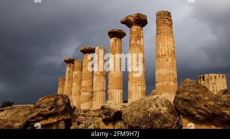 Italia, Sicilia, Agrigento, Valle dei Templi, Tempio di Eracle, rovine, colonne, resti di colonne in primo piano, luce solare calda dopo un temporale, cielo grigio nuvoloso Foto Stock
