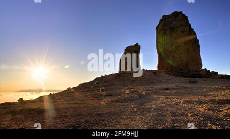 Spagna, Isole Canarie, Gran Canaria, Massiccio Centrale, montagne all'interno dell'isola, tramonto, Roque Nublo e pinnacoli vicini nella retroilluminazione, cielo blu, lava scree pendio in primo piano nella retroilluminazione, sullo sfondo sopra le nuvole si può vedere il Teide Foto Stock