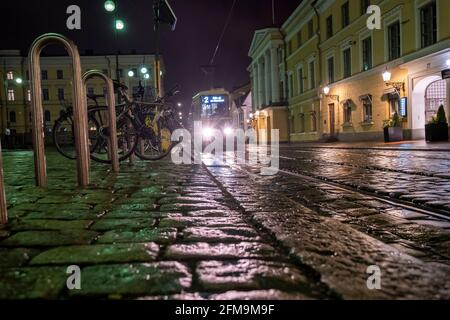 Helsinki / Finlandia - 5 MAGGIO 2021: Un tram che guida su un marciapiede in pietra bagnata nel centro di Helsinki. Foto Stock