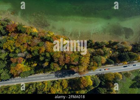 Vista dall'alto del drone di un lago con una foresta colorata in autunno e una strada nella parte inferiore della foto. Foto Stock
