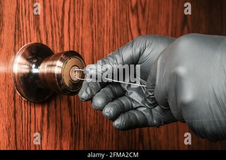 Ladro in guanti neri apre una porta di legno con una semplice serratura utilizzando un comune filo di acciaio. Concetto di protezione domestica avanzata Foto Stock