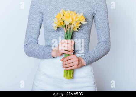 Primo piano giovane donna che tiene bouquet fresco giallo daffodil fiori mentre su sfondo bianco Foto Stock