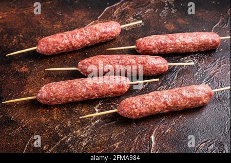 Kebab crudo di carne kofta salsicce su spiedini. Sfondo scuro. Vista dall'alto Foto Stock