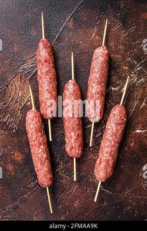 Kebab crudo di carne kofta salsicce su spiedini. Sfondo scuro. Vista dall'alto Foto Stock