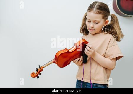 Bambina paziente con due code di pony che regola il suo supporto per violino, attaccando la lingua fuori. Indossa un abbigliamento casual a casa. Foto Stock