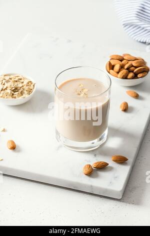 Latte di mandorle in vetro e noci su fondo bianco. Primo piano. Formato verticale. Bevanda sana senza lattosio. Mancanza di colesterolo. Foto Stock