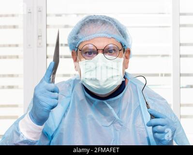 Medico in tuta protettiva che tiene un bisturi chirurgico e strumento. Il chirurgo è pronto a far funzionare il paziente. Foto Stock