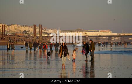 I beachgoers sulla spiaggia di Brighton durante una bassa marea, nel tardo pomeriggio, in primavera. Brighton, Sussex, Inghilterra. Brighton's Palace Pier Beyond. Foto Stock