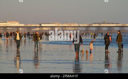 I beachgoers sulla spiaggia di Brighton durante una bassa marea, nel tardo pomeriggio, in primavera. Brighton, Sussex, Inghilterra. Brighton's Palace Pier Beyond. Foto Stock