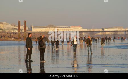 I beachgoers sulla spiaggia di Brighton durante una bassa marea, nel tardo pomeriggio, in primavera. Brighton, Sussex, Inghilterra. Brighton's Palace Pier Beyond. Foto Stock