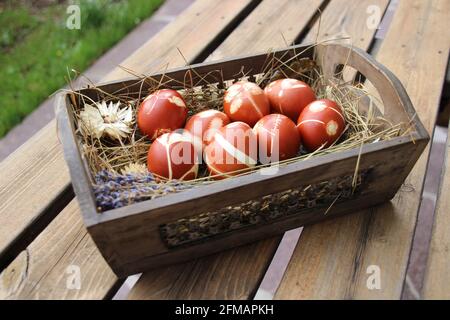 Uova di Pasqua tinte con colori naturali in un cesto pasquale con fieno, esterno, tavolo Foto Stock