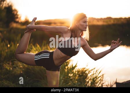 Yoga / danza posa (Natarajasana) in natura al tramonto in uno stagno, Franconia, Baviera, Germania Foto Stock