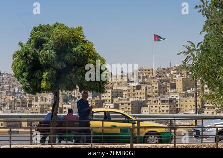 Il taxi parcheggiato su una strada ad Amman, Giordania, con uomini in piedi e seduti accanto al veicolo Raghadan flagpole visto dietro la città vecchia Foto Stock