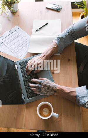 Immagine in primo piano verticale di belle mani di uomo d'affari tatuato che lavorano su un computer portatile Foto Stock