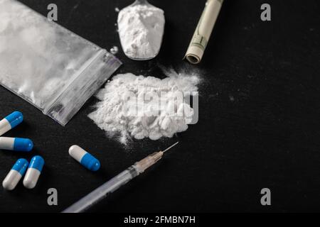 Cocaina e altre droghe su sfondo nero, primo piano. Una bolletta del dollaro arrotolata per uso della droga. Droghe proibite. Foto Stock