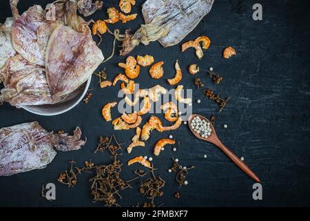 Frutti di mare secchi con calamari secchi e gamberetti secchi su a. tavolo di legno nero Foto Stock
