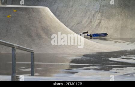 Abbandonato Blue Stunt Scooter in UN bagnato, vuoto Skate Park durante il Coronavirus Lockdown in UNA giornata piovosa. Christchurch Regno Unito Foto Stock