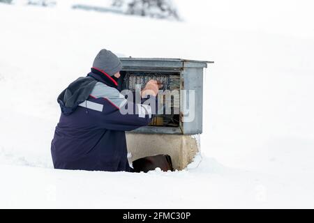 Tecnico che lavora nella neve e ripara la linea telefonica, cablaggio scatola di collegamento telefono. Foto Stock