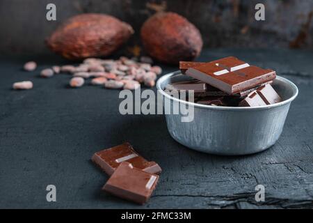 Pezzi di cioccolato fondente e fagioli di cacao sul tavolo Foto Stock