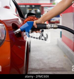 La mano del lavoratore della stazione di benzina che tiene la pompa blu del gas del benzene, riempiendo il serbatoio rosso dell'automobile di sport. Primo piano Foto Stock