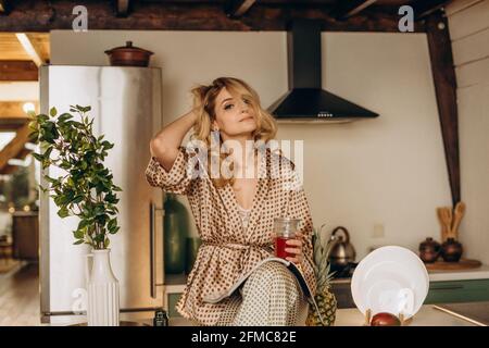 Bella donna attraente al mattino in cucina in pigiama di seta. Prima colazione romantica. Messa a fuoco selettiva, sfocatura, disturbo artistico Foto Stock