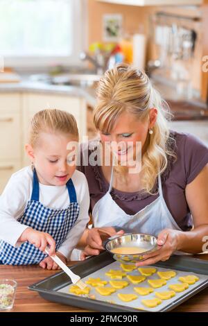 La cottura con la famiglia - madre e figlia rivestire self made cookies con una spazzola Foto Stock